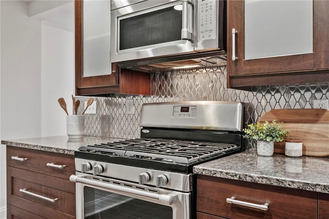 kitchen featuring tasteful backsplash, glass insert cabinets, appliances with stainless steel finishes, light stone countertops, and dark brown cabinets