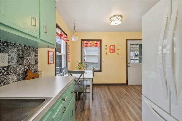 kitchen featuring baseboards, freestanding refrigerator, light countertops, light wood-type flooring, and green cabinetry