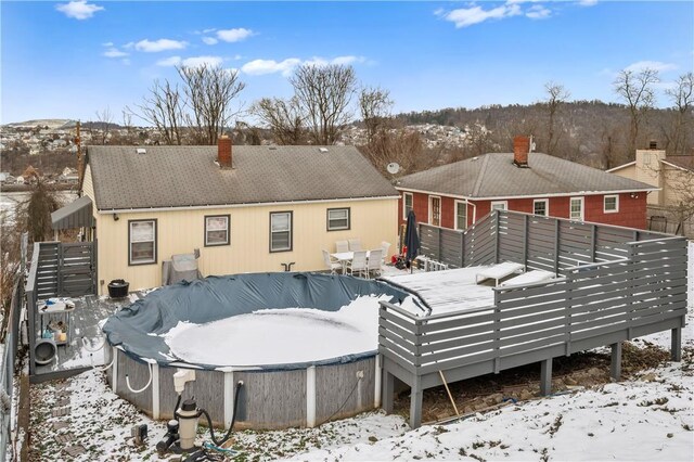 snow covered house with a covered pool, a chimney, and a deck