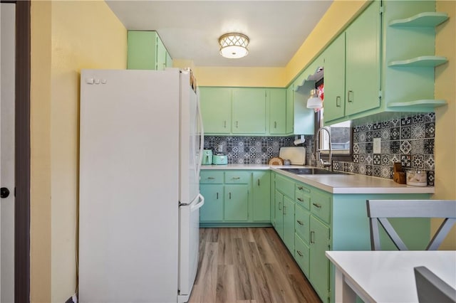 kitchen featuring open shelves, tasteful backsplash, light countertops, freestanding refrigerator, and a sink