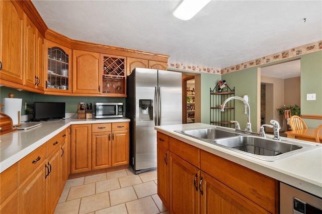 kitchen with brown cabinets, stainless steel appliances, light countertops, glass insert cabinets, and a sink