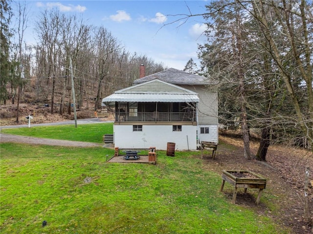 back of house with an outdoor fire pit, a lawn, and a chimney