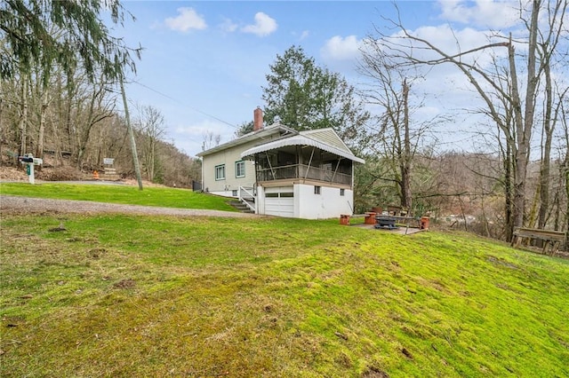 exterior space featuring a yard, a chimney, an attached garage, an outdoor fire pit, and driveway