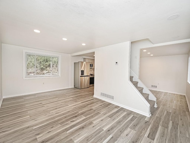 unfurnished living room featuring light wood finished floors, baseboards, stairs, and visible vents