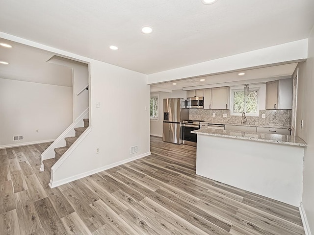 kitchen with gray cabinetry, stainless steel appliances, visible vents, backsplash, and light wood finished floors