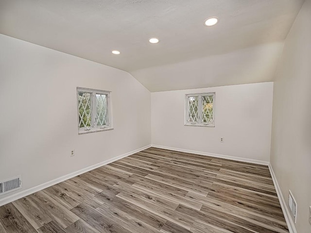 unfurnished room with lofted ceiling, plenty of natural light, visible vents, and wood finished floors