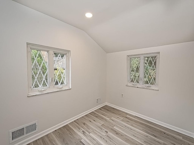 empty room featuring light wood-type flooring, baseboards, visible vents, and vaulted ceiling