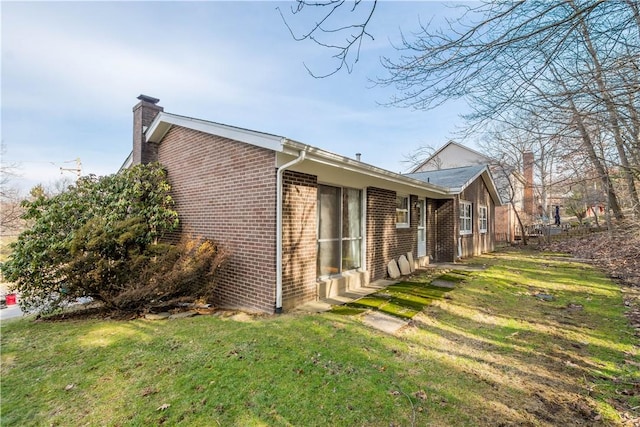 rear view of house featuring brick siding, a chimney, and a lawn