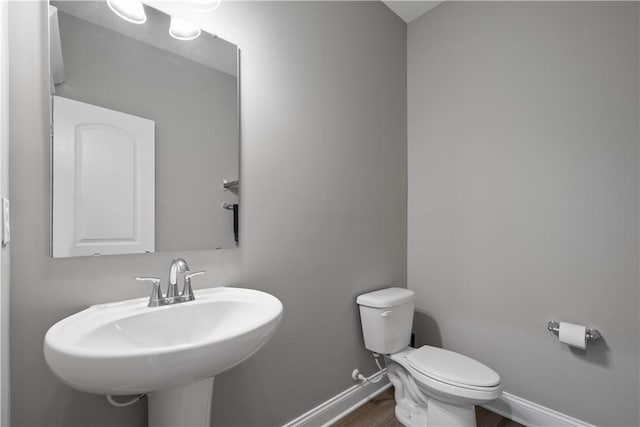 half bath featuring baseboards, a sink, toilet, and wood finished floors