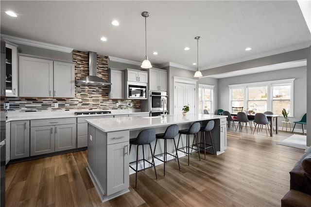 kitchen with a breakfast bar area, stainless steel appliances, gray cabinets, backsplash, and wall chimney range hood