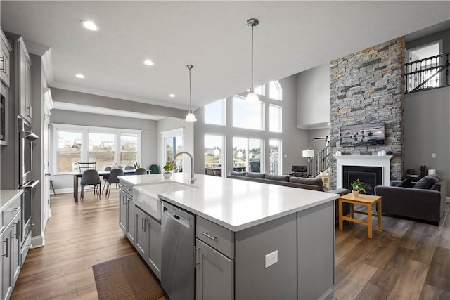 kitchen featuring wood finished floors, gray cabinetry, stainless steel dishwasher, a fireplace, and a sink