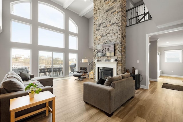 living area with a high ceiling, a fireplace, baseboards, light wood finished floors, and beamed ceiling