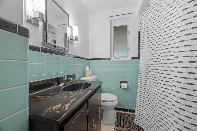 bathroom with toilet, a wainscoted wall, tile patterned floors, vanity, and tile walls