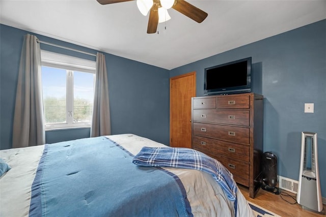 bedroom with a ceiling fan, visible vents, baseboards, and wood finished floors