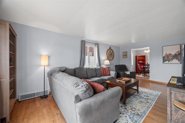 living area featuring visible vents, a notable chandelier, baseboards, and wood finished floors