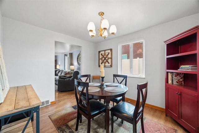 dining area featuring light wood finished floors, baseboards, visible vents, and a notable chandelier