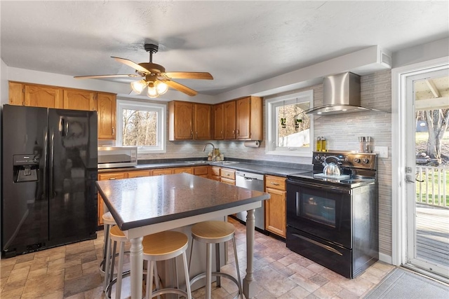 kitchen featuring a sink, wall chimney range hood, black appliances, stone finish floor, and dark countertops