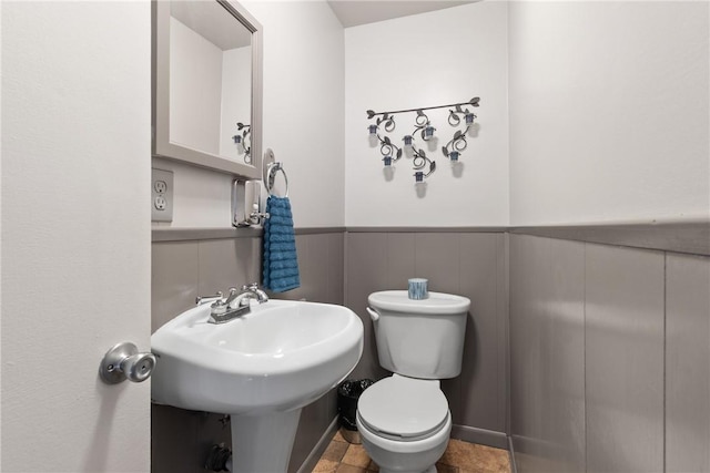 half bath featuring a wainscoted wall, a sink, and toilet