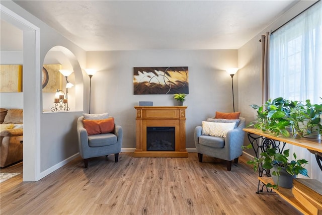 living area featuring a fireplace, light wood-style flooring, and baseboards