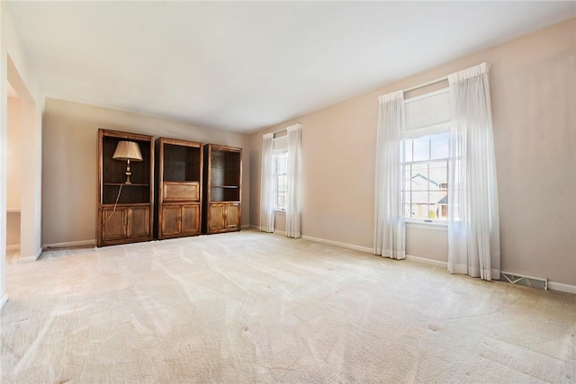 unfurnished living room with carpet floors, a healthy amount of sunlight, visible vents, and baseboards