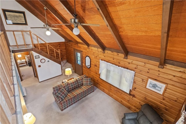 unfurnished living room with carpet, wood walls, lofted ceiling with beams, and stairs