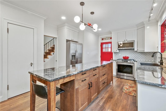 kitchen with stainless steel appliances, tasteful backsplash, ornamental molding, a sink, and hardwood / wood-style flooring