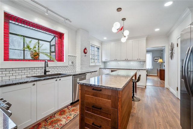 kitchen with stainless steel appliances, white cabinetry, a sink, and wood finished floors