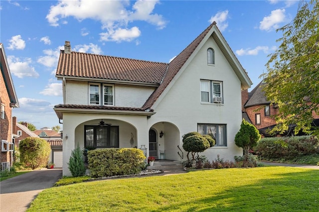 view of front of property featuring a ceiling fan, a chimney, a tiled roof, a front lawn, and brick siding