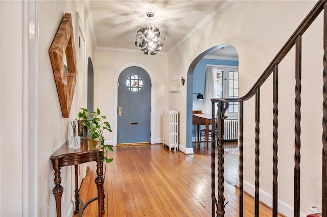 foyer entrance with arched walkways, radiator heating unit, baseboards, and light wood-style floors