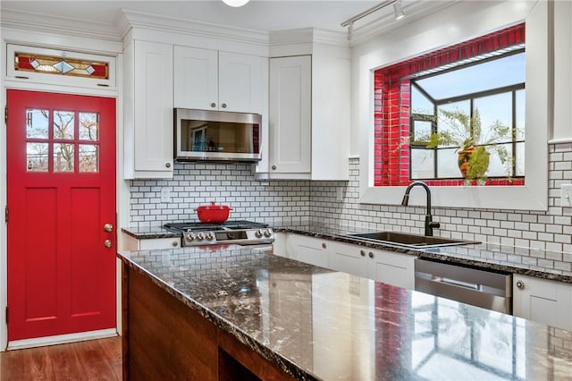 kitchen with stainless steel appliances, tasteful backsplash, white cabinets, a sink, and wood finished floors