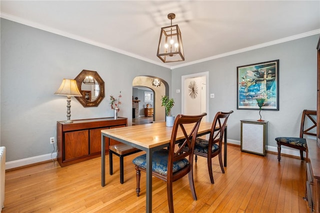 dining room with light wood-style floors, baseboards, arched walkways, and crown molding