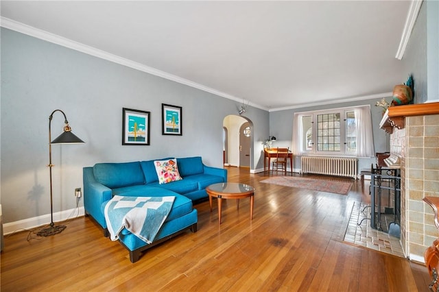 living area with arched walkways, crown molding, radiator, baseboards, and hardwood / wood-style flooring