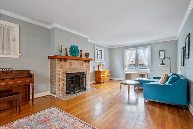 living area with radiator, ornamental molding, a tile fireplace, baseboards, and hardwood / wood-style flooring