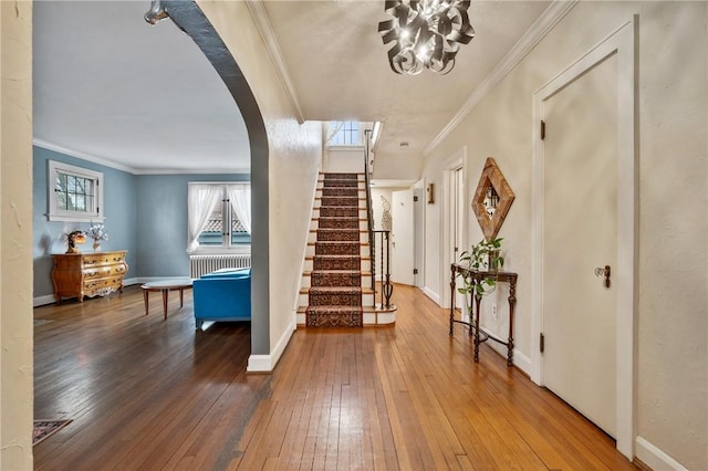 entryway featuring arched walkways, baseboards, wood-type flooring, ornamental molding, and stairs