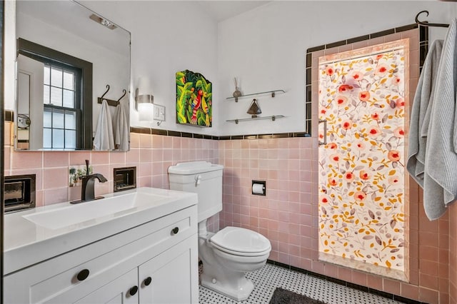 full bathroom featuring toilet, a wainscoted wall, vanity, tile walls, and a tile shower