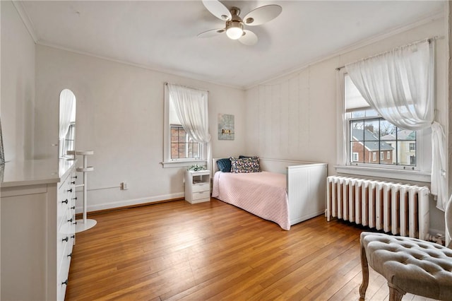 bedroom with crown molding, multiple windows, light wood-style flooring, and radiator