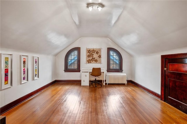 additional living space with vaulted ceiling, wood-type flooring, baseboards, and radiator