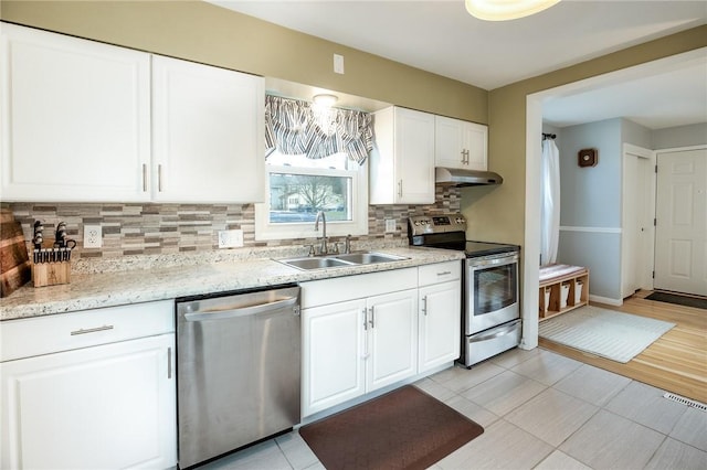 kitchen with decorative backsplash, appliances with stainless steel finishes, white cabinets, a sink, and under cabinet range hood