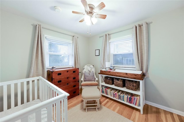 bedroom with multiple windows, a crib, baseboards, and wood finished floors