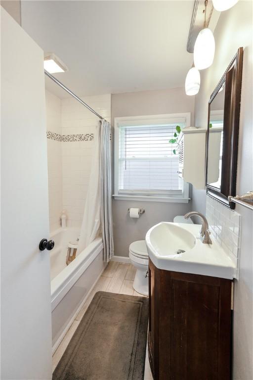 full bath featuring toilet, vanity, baseboards, decorative backsplash, and shower / bath combo