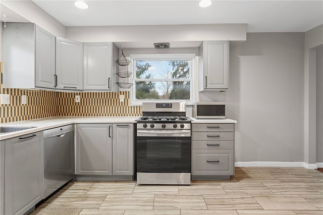 kitchen featuring stainless steel appliances, gray cabinets, light countertops, and decorative backsplash