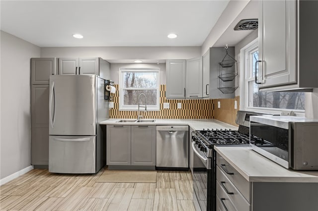 kitchen featuring stainless steel appliances, gray cabinets, light countertops, backsplash, and a sink