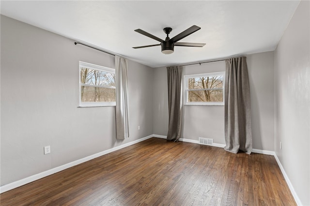 empty room with a healthy amount of sunlight, ceiling fan, visible vents, and hardwood / wood-style floors