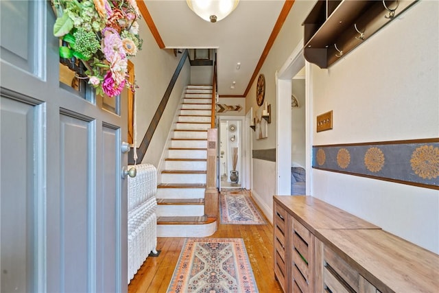 foyer entrance with stairs, light wood-style floors, a wainscoted wall, and crown molding