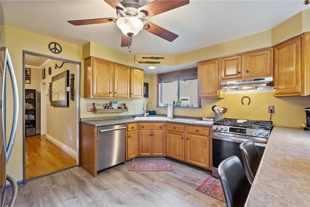 kitchen with under cabinet range hood, stainless steel appliances, a sink, baseboards, and light wood-type flooring