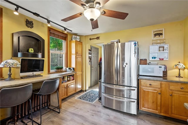 kitchen with light wood finished floors, white microwave, built in study area, and freestanding refrigerator