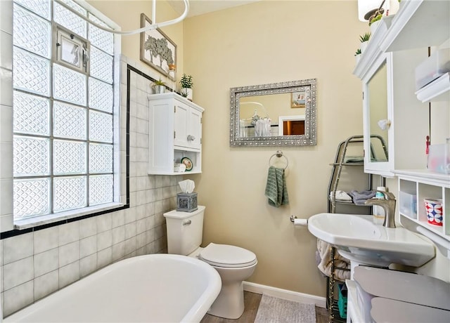 bathroom featuring baseboards, a freestanding bath, a sink, and toilet