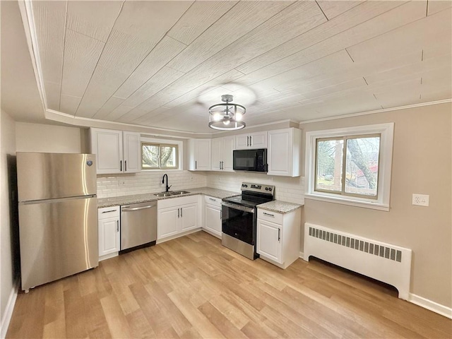 kitchen featuring radiator, light wood-style flooring, decorative backsplash, appliances with stainless steel finishes, and a sink