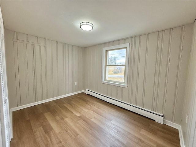 empty room featuring a baseboard heating unit, wood finished floors, and baseboards