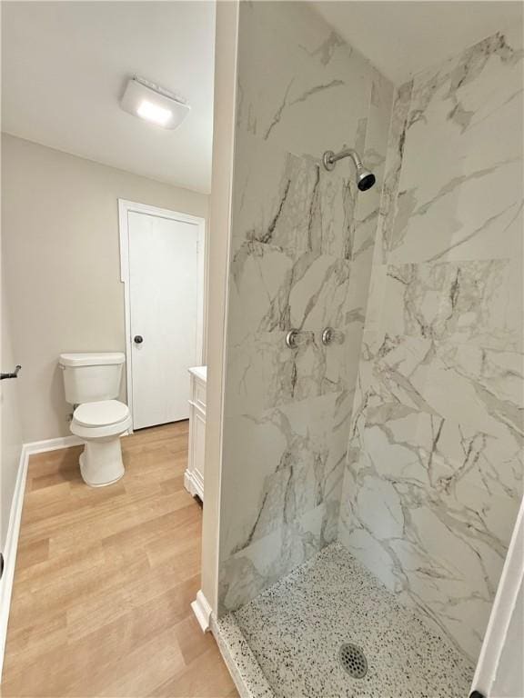 bathroom featuring a marble finish shower, toilet, vanity, wood finished floors, and baseboards